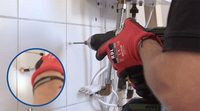 un hombre perfora la cerámica de la cocina con una broca para cerámica y un taladro.