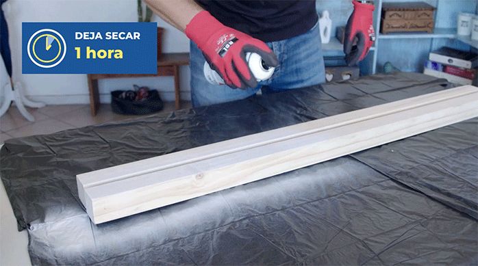 un hombre aplica pintura en spray en un trozo de pino seco cepillado para armar un gabinete para calefont