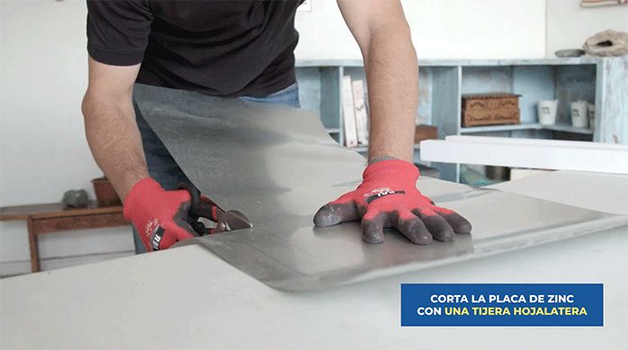 un hombre corta una plancha de zinc con una tijera hojalatera.