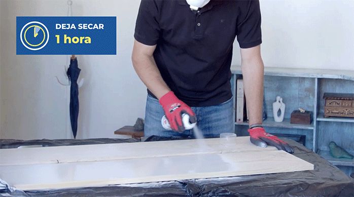 un hombre aplica pintura en spray en los trozos de terciado.