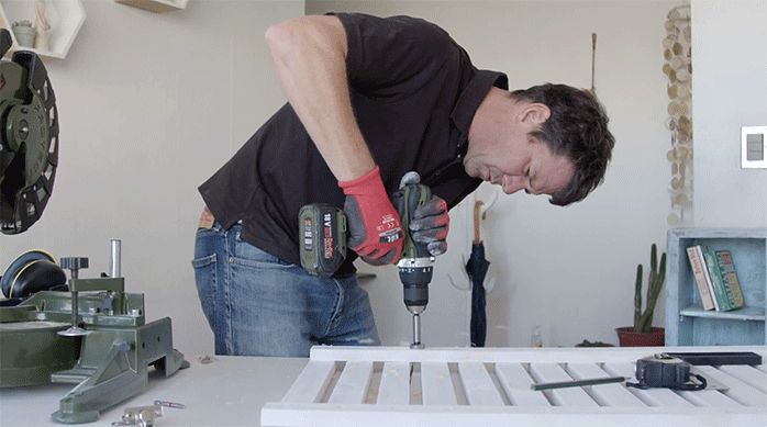 un hombre perfora la puerta del gabinete para cálefont con una brica para bisagra de 36 mm.