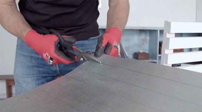un hombre corta una plancha de zinc con una tijera hojalatera.