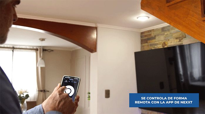 un hombre usa su smartphone para encender y apagar la ampolleta inteligente nexxt.