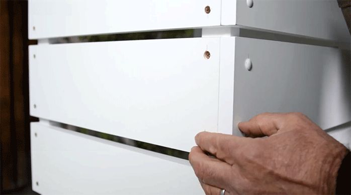 un hombre pone tapa tornillos de color blanco en todos los agujeros de los tornillos del mueble de cocina.