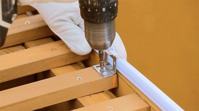 un hombre instala una fijación metálica en el cobertizo de madera para instalar el kit de techo de policarbonato alveolar.