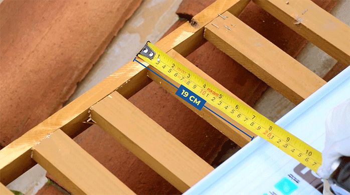 un hombre mide el espacio restante que hay que cubrir en la pérgola o cobertizo de madera.