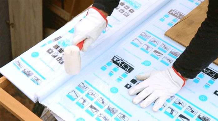 un hombre golpea con un mazo de goma sobre el perfil conector para poner el último trozo de policarbonato alveolar en el techo.