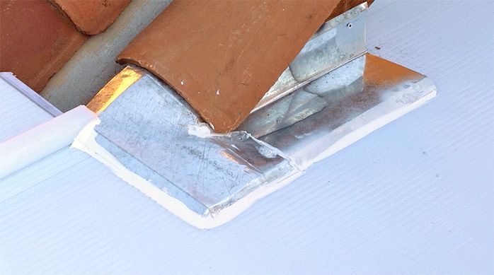 se ve el techo de policarbonato alveolar instalado y un trozo de hojalata pegado con silicona a él y a un techo de tejas para evitar filtraciones de agua.