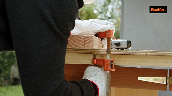 un hombre prensa un trozo de madera en un mesón de trabajo.