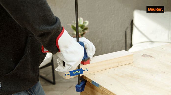 un hombre prensa un trozo de madera en un mesón de trabajo.