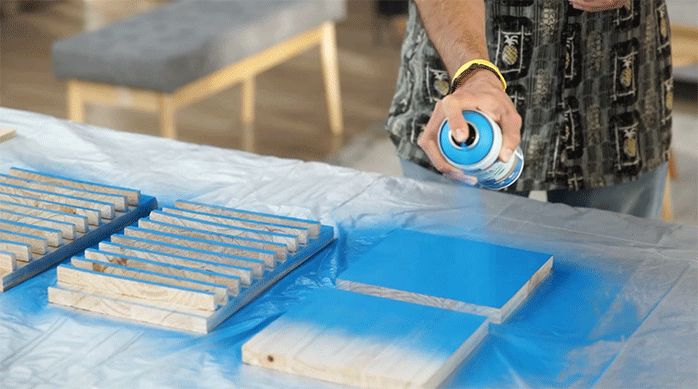 una persona aplica pintura en spray de color azul en los trozos de madera para armar el organizador gamer.