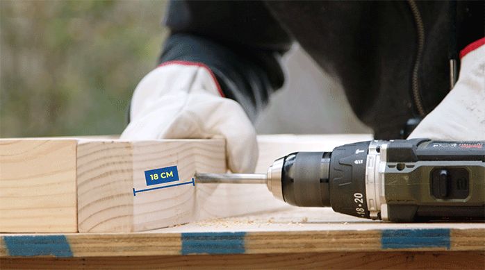 un hombre perfora un trozo de madera con un taladro y una broca.