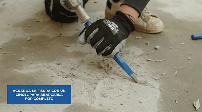 un hombre con guantes de trabajo agranda una grieta en un radier usando un cincel y un martillo.
