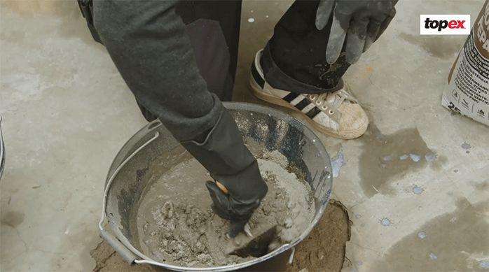 un hombre mezcla el mortero de reparación en una batea con una plana.