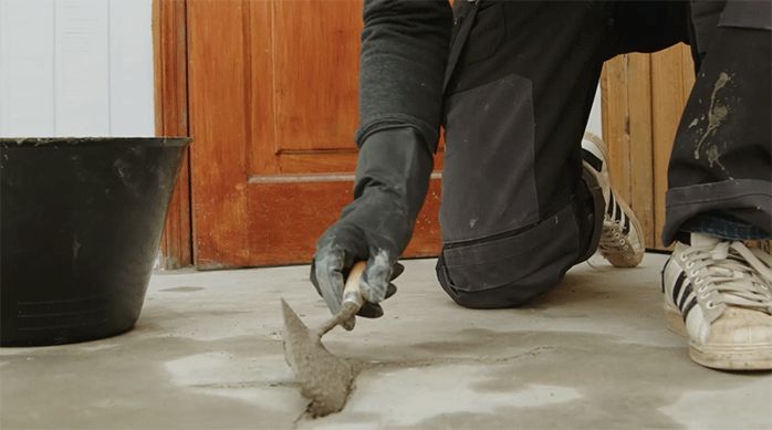 un hombre pone mortero de reparación en una fisura en un radier con una plana.