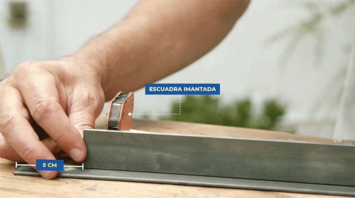 una persona sostiene una pletina en vertical sobre otra pletina y usa una escuadra imantada para sostenerla.