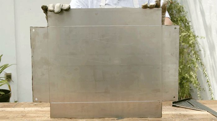 una persona muestra una plancha metálica marcada y perforada para hacer la base de la parrilla de pared.