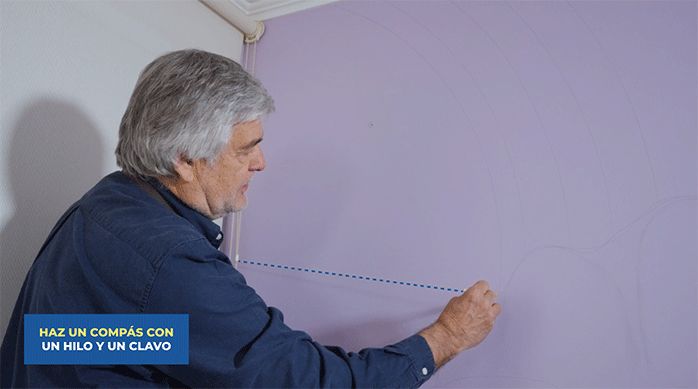 un hombre traza una figura circular en el muro del rincón de lectura con un hilo y un clavo.