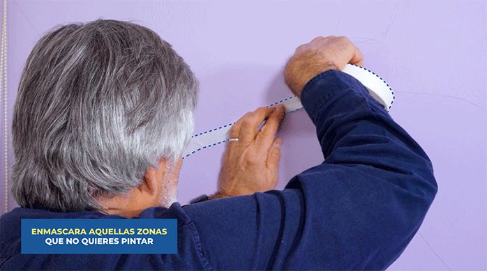 un hombre pone cinta para enmascarar en el diseño del mural para luego pintar.