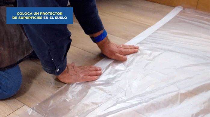 un hombre pone un protector plástico en el piso para no ensuciarlo al pintar el mural.
