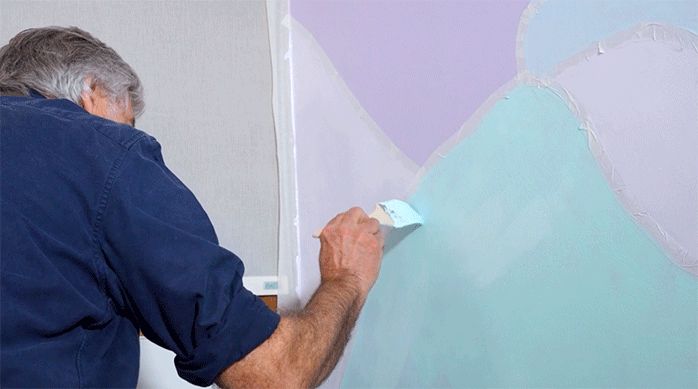 un hombre pinta el mural del rincón de lectura con colores pasteles.