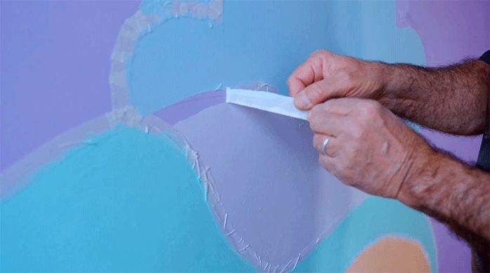 un hombre retira la cinta para enmascarar del mural para develar el diseño.