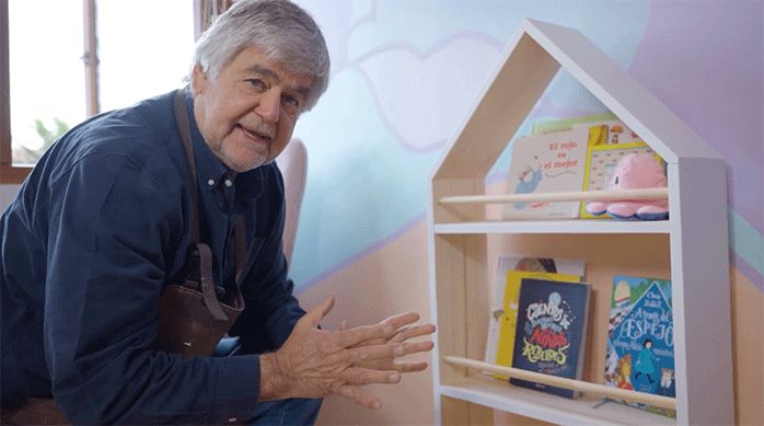 un hombre muestra el rincón de lectura infantil terminado.Se ve el librero con diferentes libros para niños.