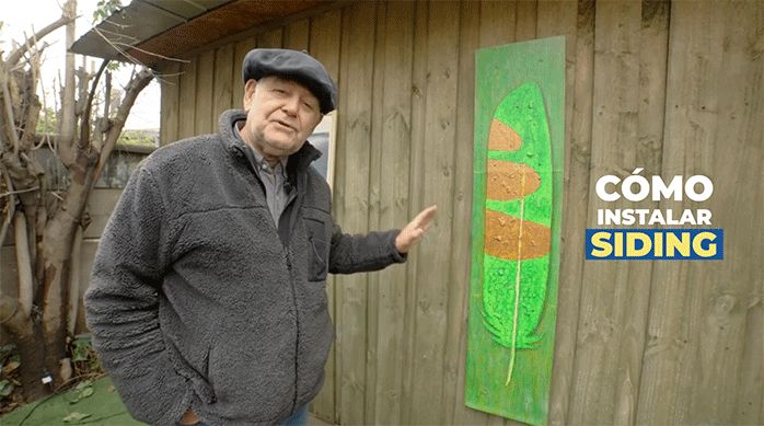un hombre frente a una casa de madera listo para explicar cómo instalar siding en ella.