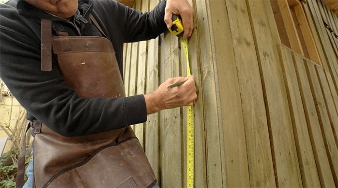 un hombre mide la altura para instalar super fieltro en una casa con una huincha de medir.