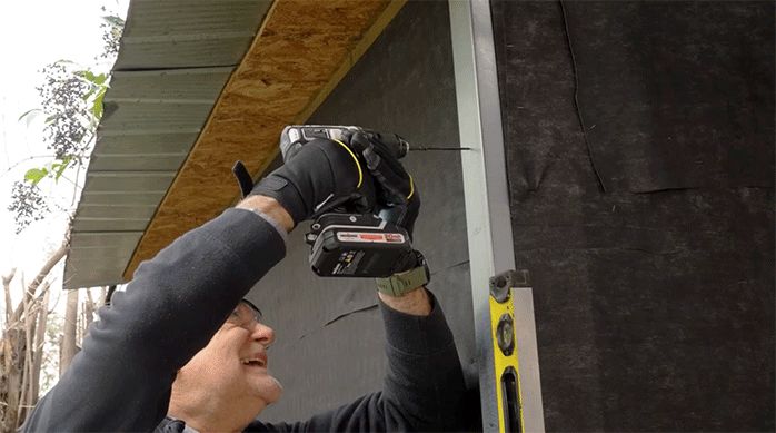 un hombre fija un perfil de metalcon como pilar en la pared exterior de una casa.