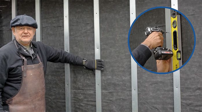 un hombre muestra los perfiles de metalcon recién instalados como pilares en las paredes exteriores de una casa.