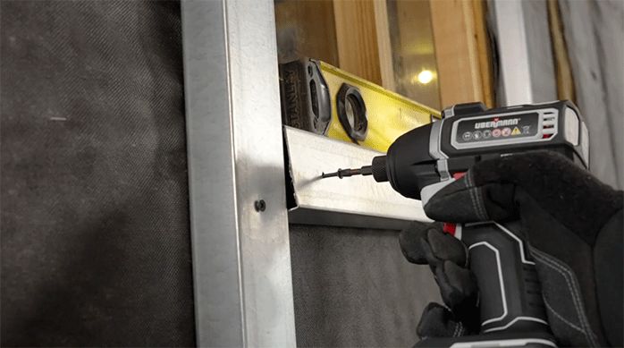 un hombre fija un perfil de metalcon bajo la ventana de la casa.