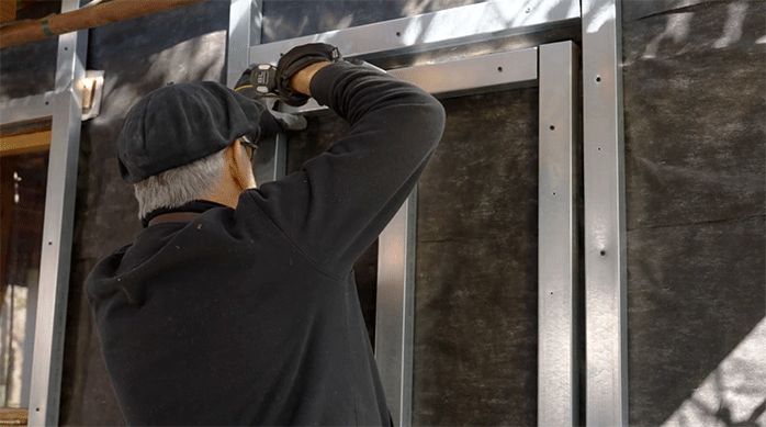 un hombre fija perfiles de metalcon por todo el marco de la puerta de la casa.