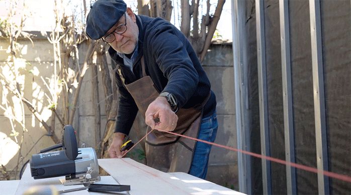 un hombre usa un tizador para marcar una medida en una plancha de siding.