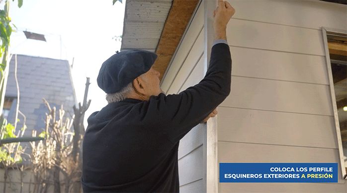 un hombre presiona el esquinero sobre los perfiles j en la esquina de la casa para fijar la unión.