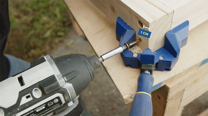 una persona fija una esquina del marco de madera con tornillos y una prensa esquina.