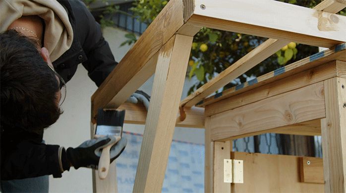 una persona aplica barniz para proteger la madera del alero.