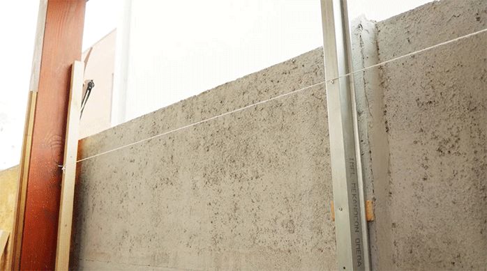 un muro de concreto con pilares de madera y un pilar de pino seco cepillado con un clavo y una lienza. Al medio hay un pilar de metalcon.