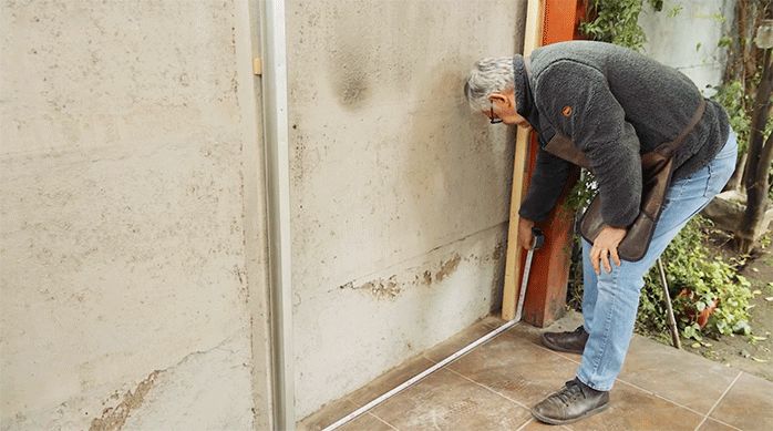 un hombre mide el largo de un espacio en que va a instalar siding en un quincho.