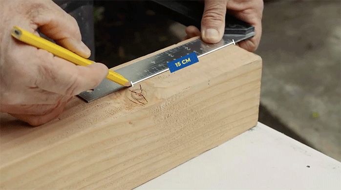 una persona marca 15 cm en un trozo de madera con una regla y un lápiz.