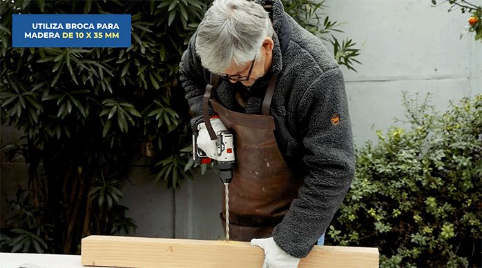 un hombre perfora un trozo de madera con una broca para madera de 10 x 35 mm.