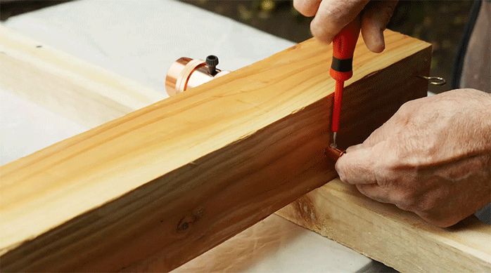 un hombre instala una luminaria en un trozo de madera barnizado.
