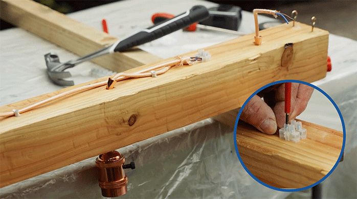 una persona fija los cables de una lámpara para colgar en un trozo de madera.