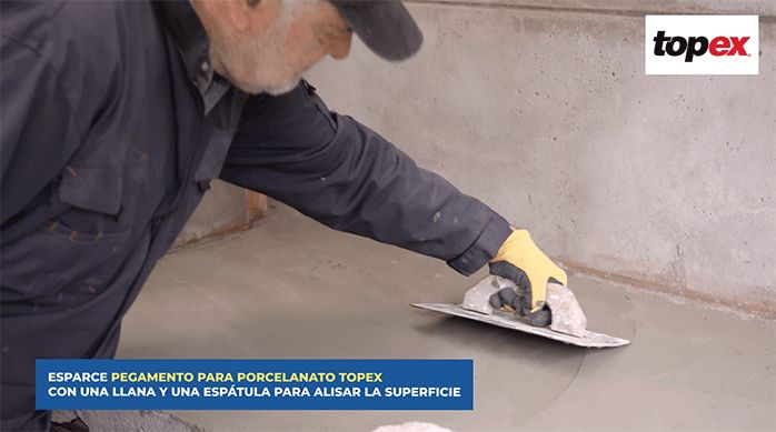 un hombre usa una llana para emparejar pegamento para porcelanato en un mesón de un quincho.