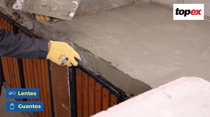 una persona con guantes de trabajo aplica pegamento para porcelanato con una espátula para nivelar los mesones de un quincho.