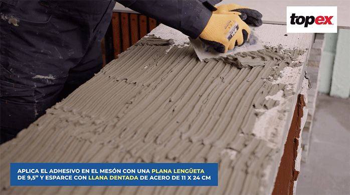 una persona aplica el adhesivo para porcelanato en un mesón de un quincho con una llana dentada.