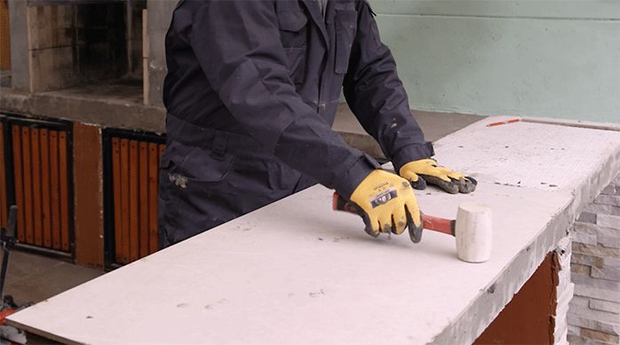 un hombre usa un mazo de goma para asentar la plancha de porcelanato en el mesón.