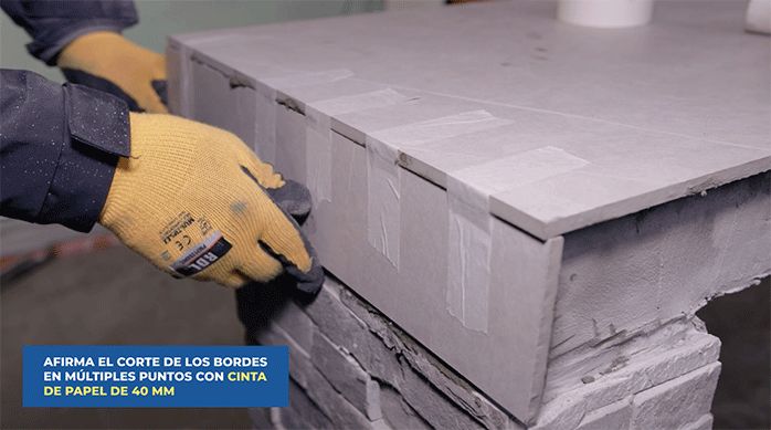 un hombre pega un trozo de porcelanato en el extremo del mesón del quincho y lo sujeta con cinta para enmascarar.