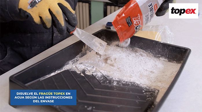 una persona mezcla el fragüe con agua en una bandeja usando una espátula.