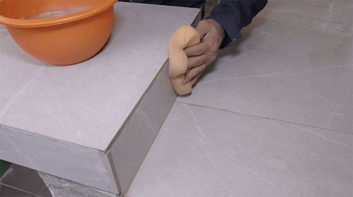 una persona pasa una esponja húmeda para limpiar el polvo del fragüe y dejar el porcelanato impecable.